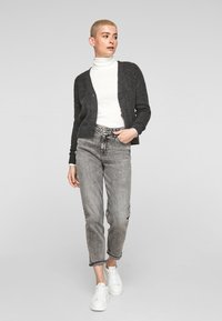 Gilet tricoté gris foncé avec fermeture à boutons, associé à un jean gris taille haute et des baskets blanches. Texture et coupe lisses et décontractées.