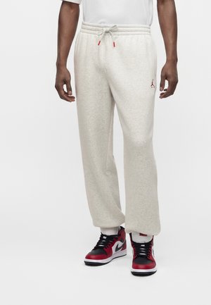 Mann trägt hellbeige Sweathosen mit Kordelzug und roten und schwarzen Nike-Sneakers auf weißem Hintergrund.