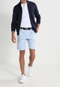 Námořnický kardigan na zip, bílá polokošile, světle modré kraťasy, černý pásek a bílé tenisky. Ležérní outfit s čistými liniemi a jednoduchými barvami.