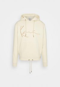 Krémová mikina s kapucí a přední kapsou, se zlatými šňůrkami a kurzivní logem. Obsahuje žebrované manžety a uvolněný střih. Měkký materiál z bavlněné směsi.