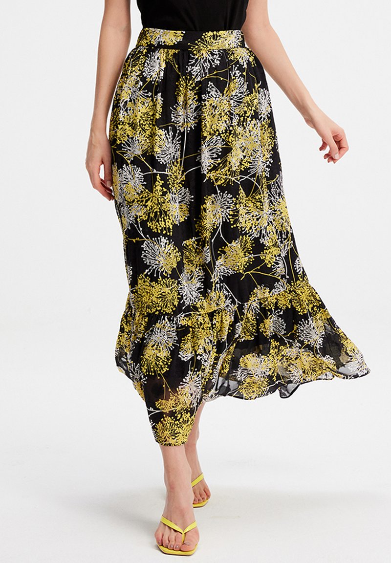 Jupe maxi florale noire avec des motifs de fleurs jaunes et blanches, fabriquée en tissu léger, dotée d'un ourlet volanté et d'une ceinture à la taille.