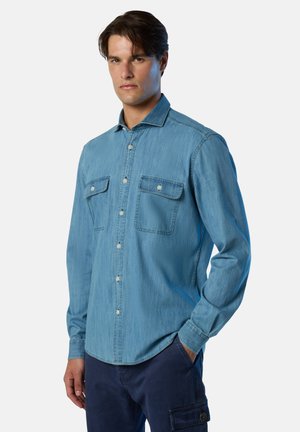 Camicia in denim blu chiaro con chiusura a bottoni, due tasche sul petto e colletto classico. Maniche lunghe con polsini abbottonati. Texture liscia.