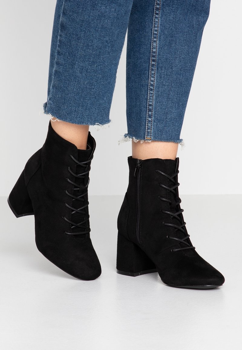 Stivali ankle in suede neri con punta appuntita, chiusura a lacci sul davanti e zip laterale. Tacco chunky con superficie testurizzata.