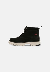 Botines de ante negro con suela de goma beige, punta redonda, diseño de cordones y una lengüeta en la parte posterior. Acento del logo rojo en el lateral.