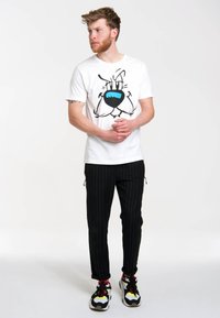 White cotton t-shirt featuring a graphic design of a character with blue accents. Black pinstripe pants and multi-colored sneakers complete the look.