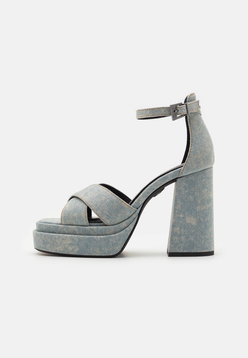 Kang sandalsi denimu sa cross-strap dizajnom, blok petom, kaišem oko gležnja i svijetloplavom bojom, sa suptilnom ispucanom teksturom.