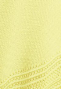 Tissu tricoté jaune avec un motif complexe façon dentelle le long du bord inférieur, montrant une couture fine, détaillée et une texture.