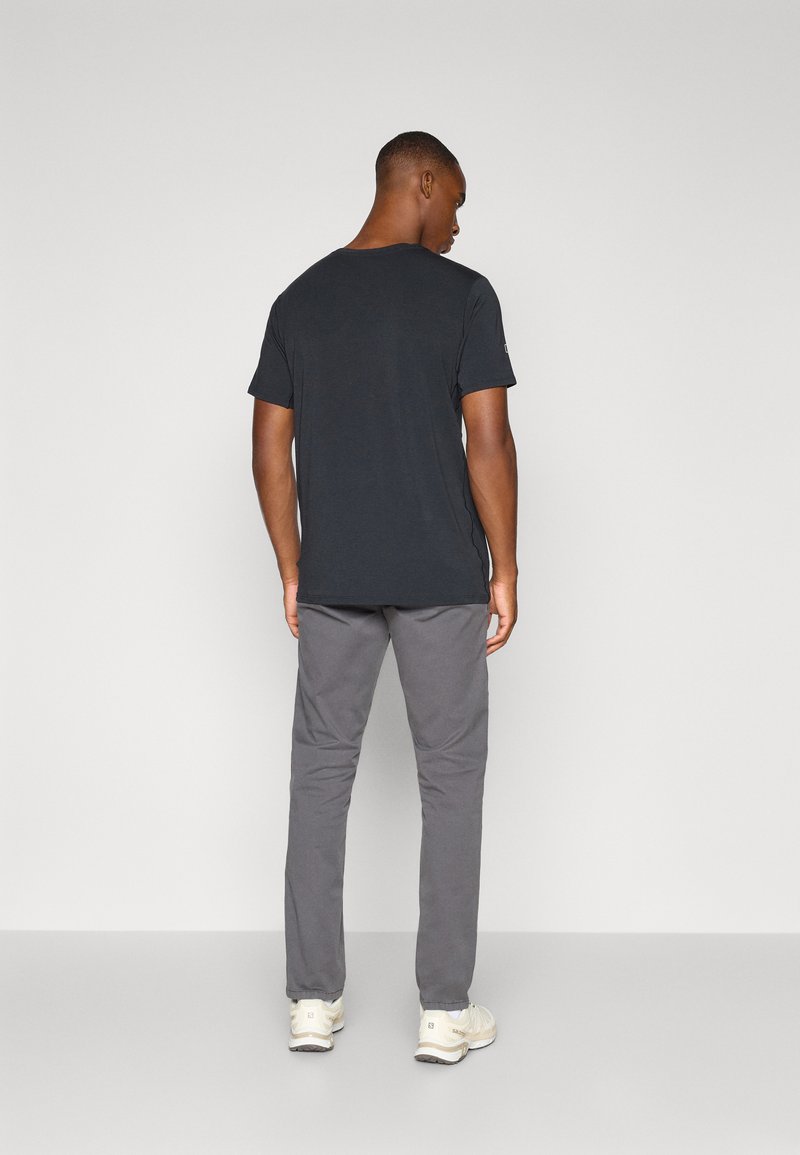 Graues T-Shirt mit normaler Passform und Rundhalsausschnitt, kombiniert mit grauen Hosen. Die Rückseite des Shirts zeigt eine einfache, glatte Textur.