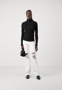 Mustmustriibuline turtleneck sviiter, valged kulunud laiad püksid, must tekstureeritud käsitasku kuldse kettiga ja mustad terava nina kingad.