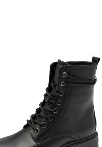 Čierne kožené členkové topánky na šnurovanie s kovovými očkami, textúrovaným povrchom, pútkom a hrubou podrážkou pre zvýšenú odolnosť.