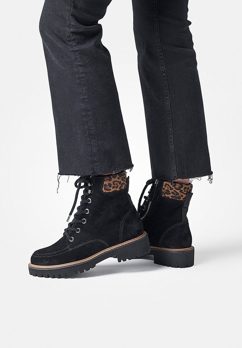 Bottines en suède noir avec un accent en imprimé léopard texturé, lacets à l'avant et semelle en caoutchouc robuste. Jeans noirs avec ourlet déchiré visibles.
