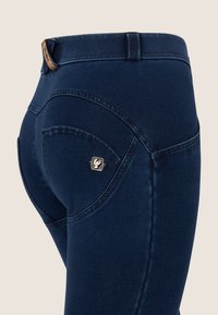 Tummansiniset farkut, joissa on korkea vyötärö, kaarevat taskut ja pieni metallinen logotunnus takataskussa.