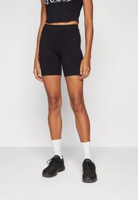 Svarte ribbestrikkede sykkelshorts med høy midje, kombinert med en svart cropped topp. Modellen har på seg svarte joggesko og hvite ankelstrømper.
