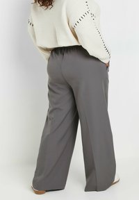 Grå vida byxor med elastisk midjeband, med sidofickor och ett mjukt, lätt tyg. Texturen verkar vara mjuk och följsam.