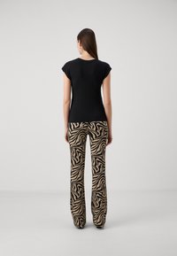 Top negro de manga corta combinado con pantalones de tiro alto en color beige que presentan un patrón de cebra negro. Telas suaves, ajuste relajado y diseño de pierna acampanada.