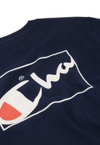 Camisa de algodón azul marino con un gran logotipo blanco y rojo en un diseño rectangular. La tela parece suave y tiene un escote redondo clásico.