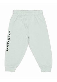 Pantalon de survêtement gris clair avec une ceinture élastique, des poignets resserrés et un logo noir "JORDAN" imprimé sur la jambe gauche. Texture de tissu douce.