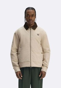 Giacca bomber beige con colletto in velluto a coste, zip frontale, tasche laterali e logo ricamato sul petto. Tessuto dalla trama liscia.