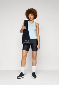 Light blue sports tank top, black compression shorts, black towel over shoulder, white socks, and black athletic shoes with gray accents.