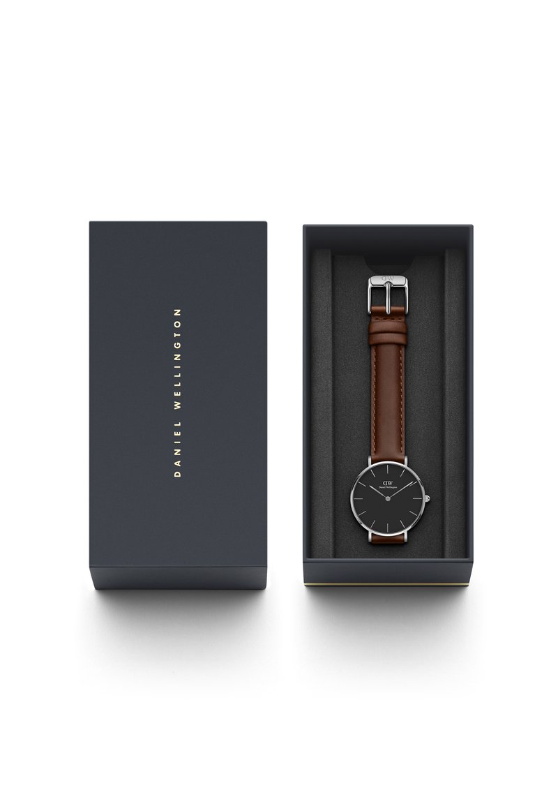 Orologio rotondo con quadrante nero, hardware argento e cinturino in pelle marrone, presentato in una scatola blu navy con scritte dorate. Fodera interna morbida.