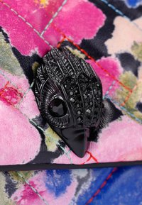 Tessuto colorato quilted con sfumature di rosa e blu, con un ornamento a forma di uccello nero decorato con cristalli.