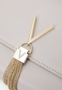 Borsa grigia con texture, caratterizzata da un accento in metallo dorato con logo "V" e una nappina realizzata con catene dorate intrecciate.