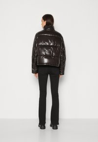 Chaqueta de plumas negra y brillante con un diseño recortado y cuello alto. Presenta paneles acolchados y un acabado brillante. Combinada con pantalones acampanados negros.