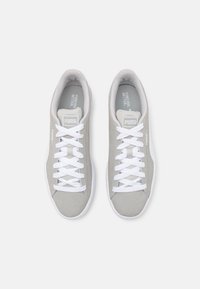 Heledad hallid spordijalatsid suede tekstuuriga, valged paelad ja valged kummist tallad. Omab bränditud keelt ja minimalistlikku disaini.