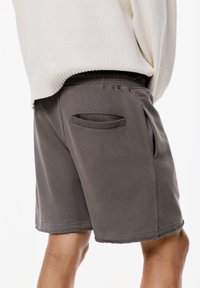 Graue Sportshorts mit einem elastischen Bund, ausgestattet mit zwei Seitentaschen und einem rohen Saum. Der Stoff wirkt weich und hat eine glatte Textur.