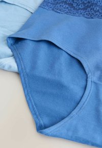 Niebieskie bawełniane ubrania nałożone na siebie; jedno z nich ma teksturowany koronkowy górny materiał, natomiast drugie ma gładkie wykończenie. Szycia są widoczne wzdłuż krawędzi.