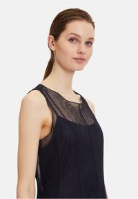 Robe sans manches en tissu bleu marine avec une superposition en maille transparente au niveau du col, présentant un col rond simple et une coupe ajustée.