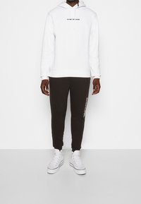 Vit hoodie med ficka fram och logo, kombinerad med svarta joggerbyxor med sidoförtryck och vita högskor. 