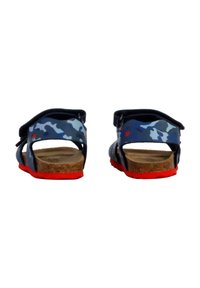 Sandali per bambini in camouflage blu con accenti a forma di stella rossa, suole in sughero marrone e suole di un brillante rosso, visti da dietro.