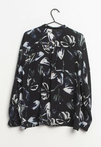 Blusa nera a maniche lunghe con grandi motivi floreali bianchi e grigi appesa a una gruccia nera su uno sfondo bianco.