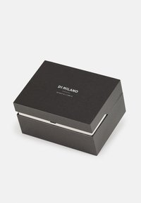 Boîte en carton noir avec une surface texturée, présentant un logo blanc "DI MILANO" sur le dessus. Le design est rectangulaire avec un couvercle à charnière.