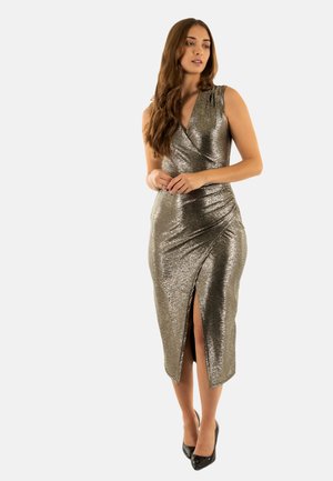 Abito avvolgente in argento metallico con uno spacco alta alla coscia, design senza maniche, arricciatura su una spalla e una texture liscia. Abbinato a tacchi neri.