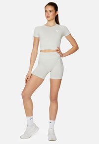 Light gray athletic set featuring a fitted crop top and high-waisted shorts. Smooth fabric with logo detail on both pieces. White sneakers and socks.