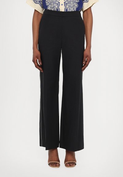 Pantaloni neri a gamba larga con vita alta, caratterizzati da una texture liscia e dettagli sulle cuciture laterali. Abbinati a un top con fantasia e scarpe open-toe.