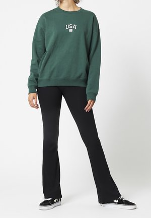 Groene sweatshirt met "USA" logo, ribbelboord bij de crewneck en cuffs. Gecombineerd met zwarte ribbel flared pants en zwarte sneakers.