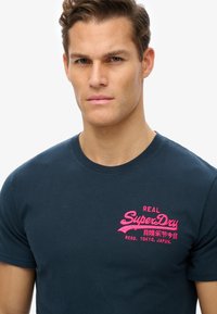 Camiseta de algodón de color marino con cuello redondo, mangas cortas y un destacado bordado rosa en el pecho. Corte regular.