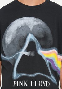 Musta puuvillapaita, jossa on Pink Floydin logo. Pyöreä graafinen kuvasto, jossa on prisma ja sateenkaaren värit, pehmeä texture ja rohkeat kontrastivärit.