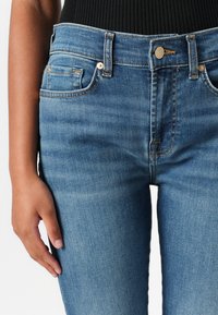 Fitted blauwe denim jeans met een middelhoge taille, vijf zakken en gouden stiksel details langs de naden. Geweven stof met een lichte vervaging.