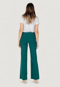 Pantaloni a zampa d'elefante verdi con vita alta, realizzati in un tessuto liscio e leggero. Abbinati a una camicia bianca a maniche corte.