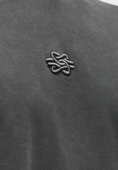 Σκούρο γκρι ύφασμα με απαλή υφή, που διαθέτει ένα έντονο κεντημένο σχέδιο κόμπου στο ίδιο χρώμα κλωστής.