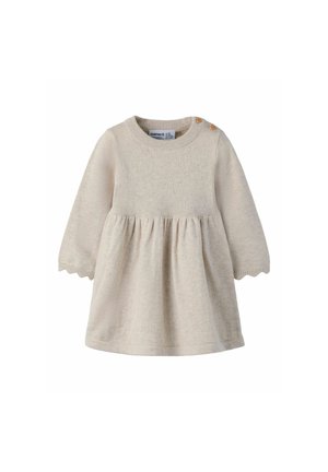 Robe bébé longue beige en tricot avec deux boutons en bois sur l’épaule et bords festonnés aux poignets.