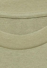 Svijetlozeleni dukserica materijal s strukturiranom završnom obradom, s rebrastim izrezom oko vrata i glatkim detaljima šivanja.