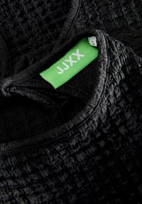 Zwart textiel met een geweven patroon. Heeft een ronde halslijn en een groen label met "JJXX" en maat "S."