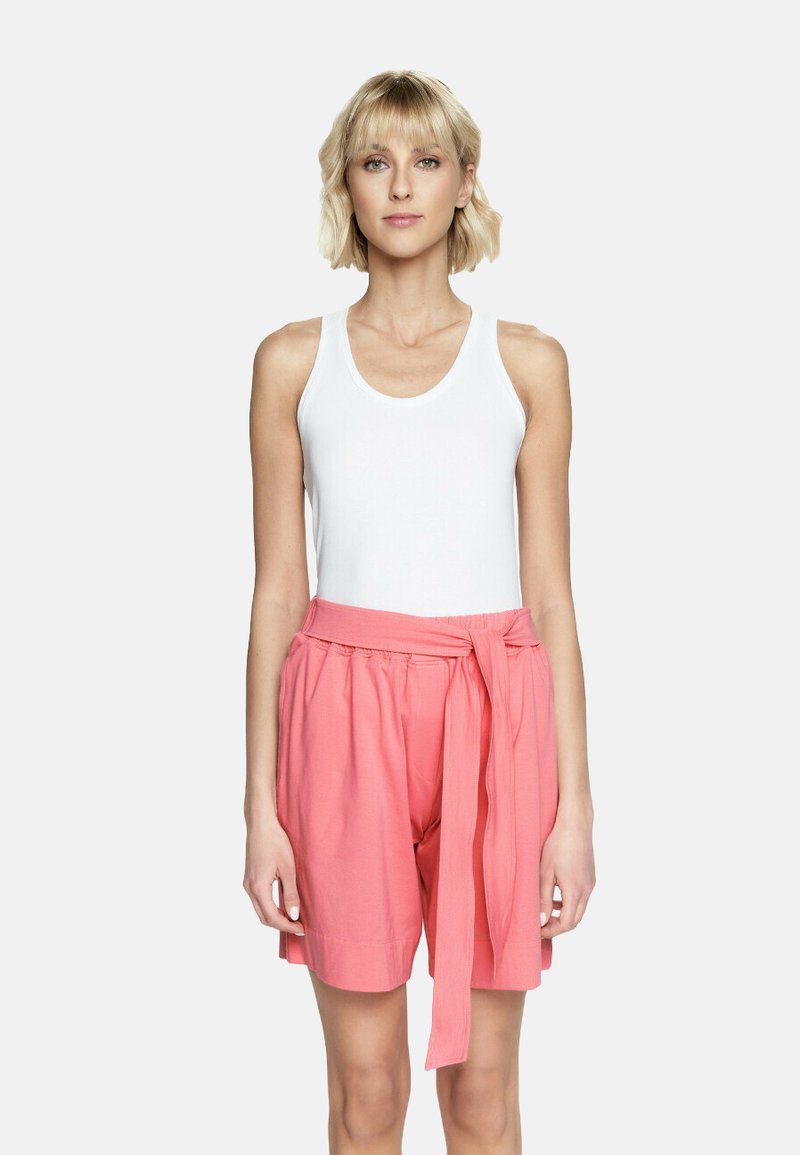 Biały top na ramiączkach w połączeniu z szortami w kolorze koralowym, sięgającymi do kolan, z wiązanym paskiem, wykonanymi z miękkiego materiału, o luźnym kroju i marszczonym pasie.