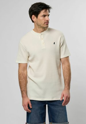 Light beige short-sleeve henley shirt with a textured weave, three-button placket, and a small black logo on the chest.