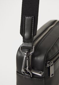 Black leather bag featuring a textured finish, a durable strap, and metal hardware details, including a zipper and logo accent.